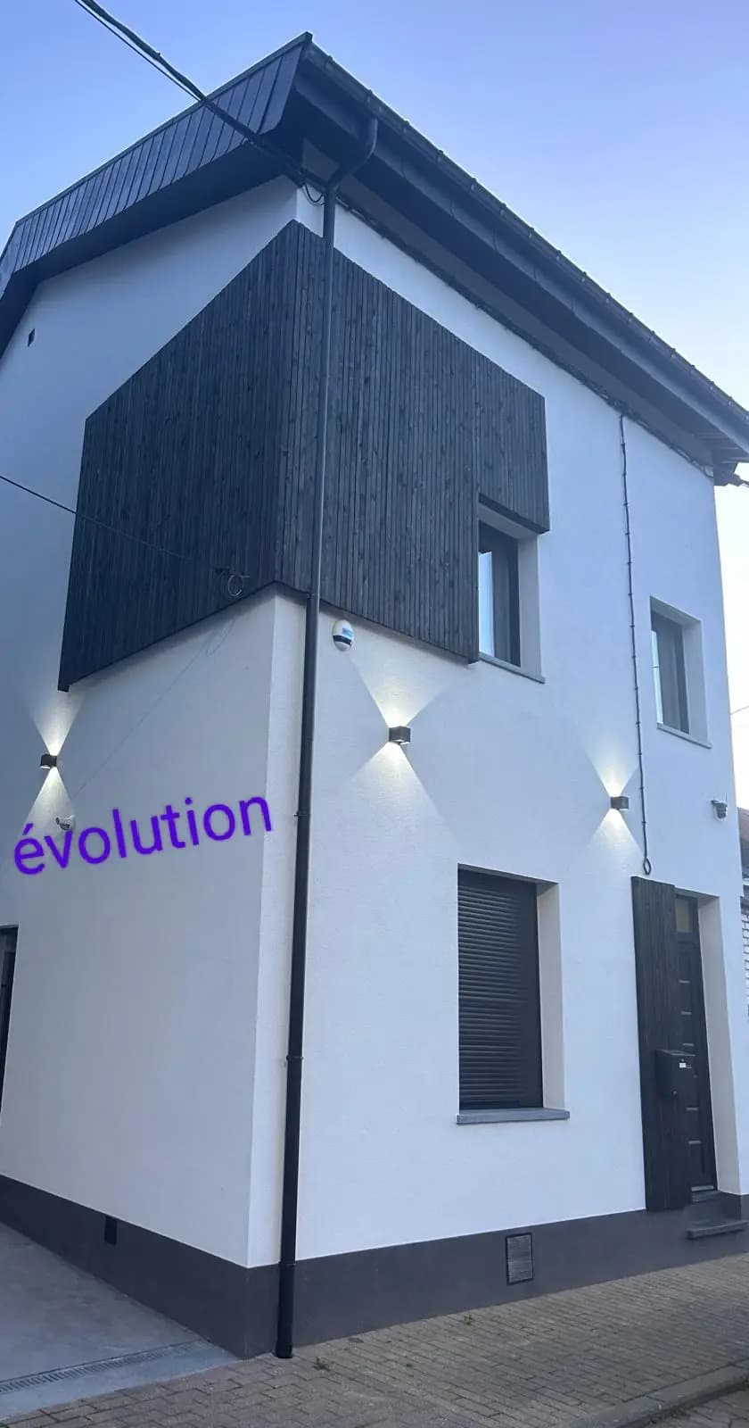Maison à façade crépie blanche avec bardage sombre et éclairages extérieurs