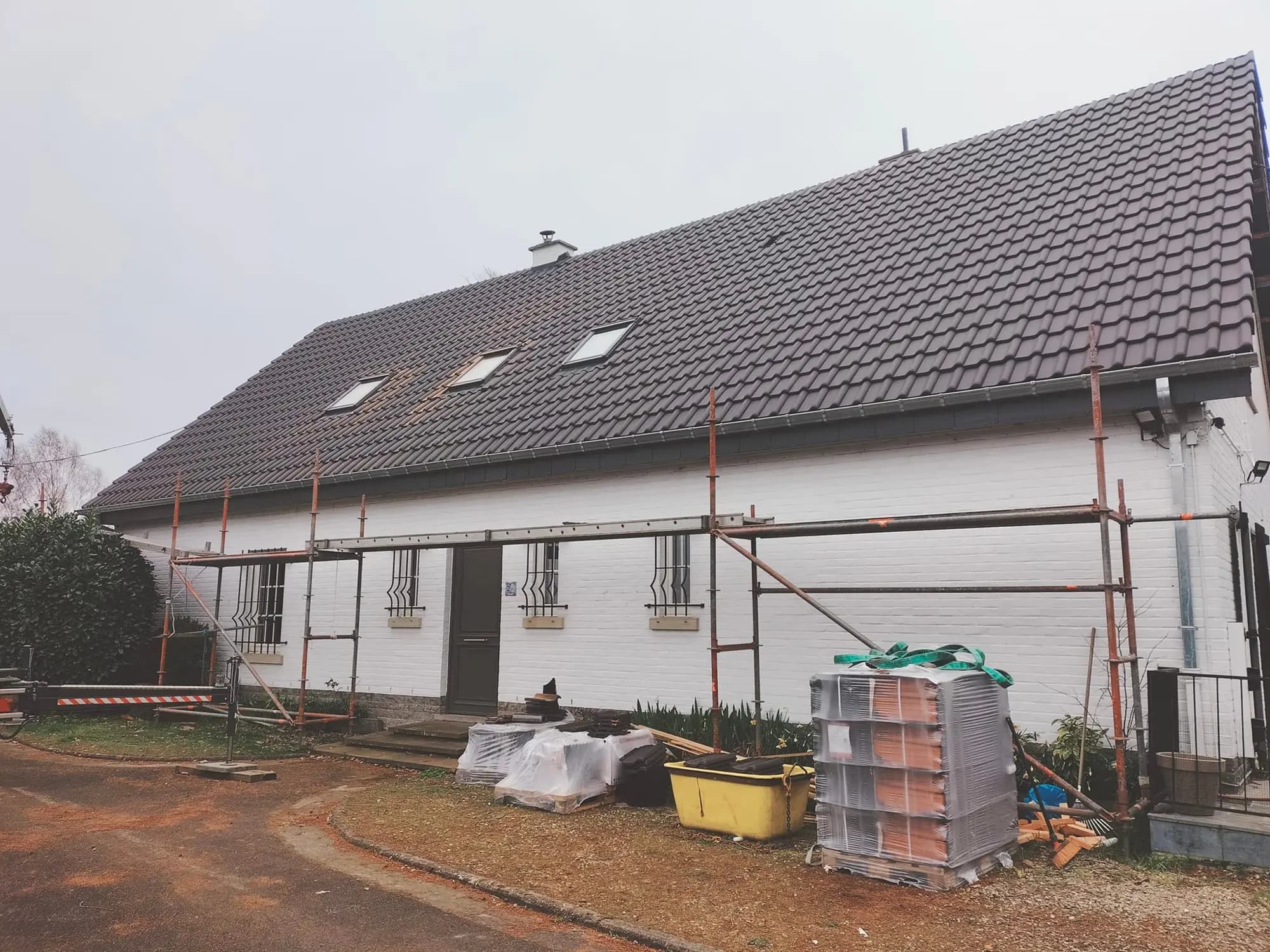 Longue toiture en tuiles avec échafaudage monté le long de la façade blanche